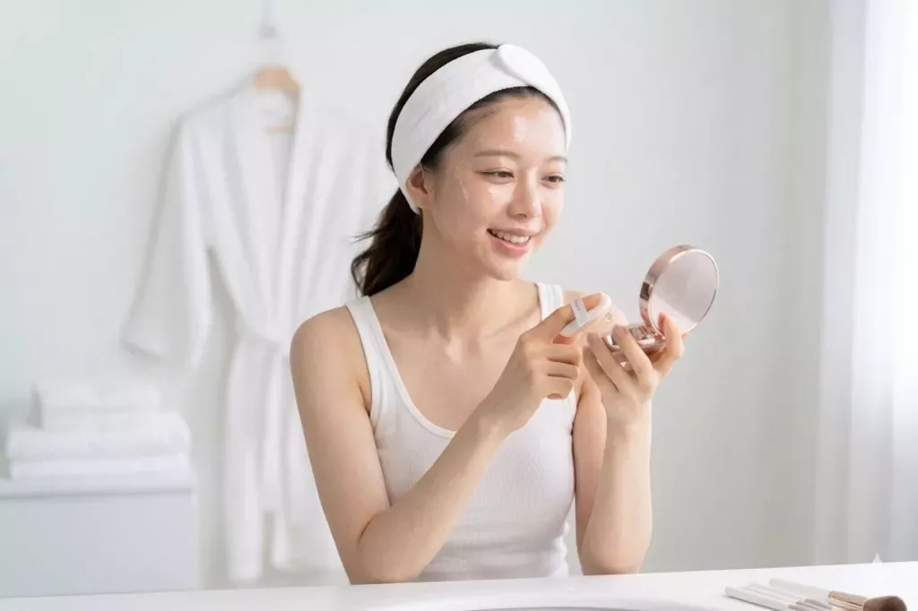 K-Beauty Cushion Foundation Guide: How to Get That "Filter-In-A-Compact" Glow 1 A young woman with radiant glass skin applying makeup using the **K-Beauty Cushion Foundation Guide** technique for a flawless, natural look.